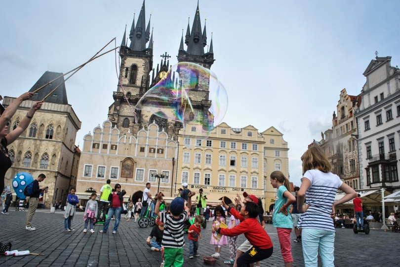 Children in Old Town Square try to pop big bubbles as they float over their heads.