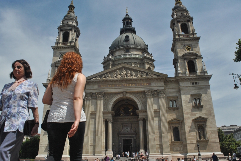 Two women wander around St. Stephen's Basilica, one walking toward it and the other away from it.